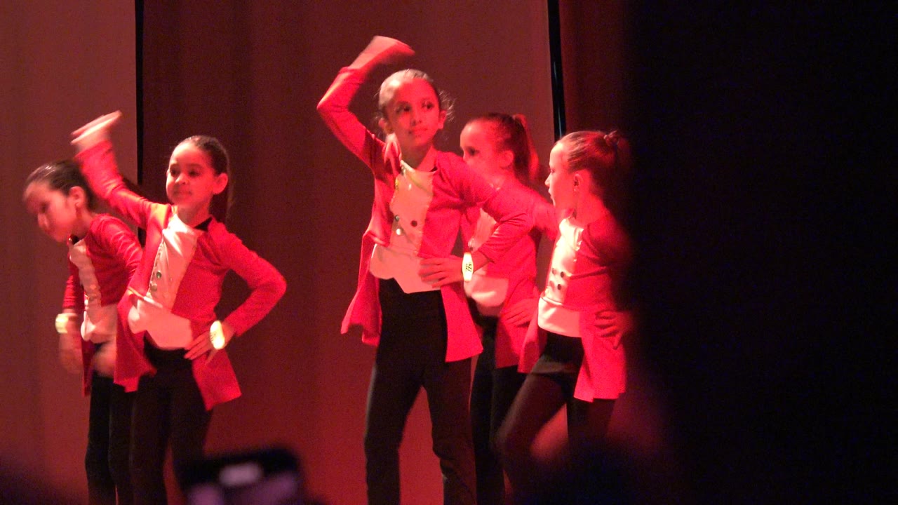 Girls in red costumes pose and move during a stage routine.