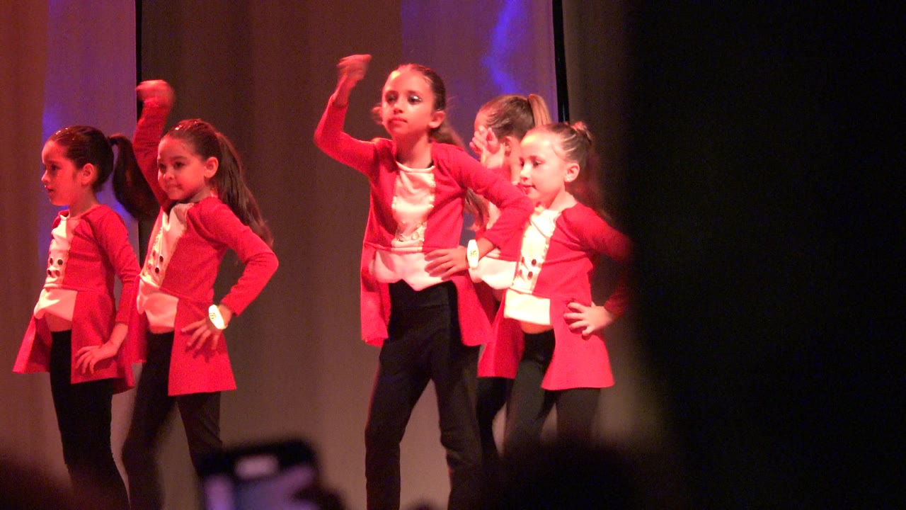 Children in matching red jackets stand in a stage formation in San Jose del Cabo BCS Mexico, with hands on hips and warm red light across the scene.