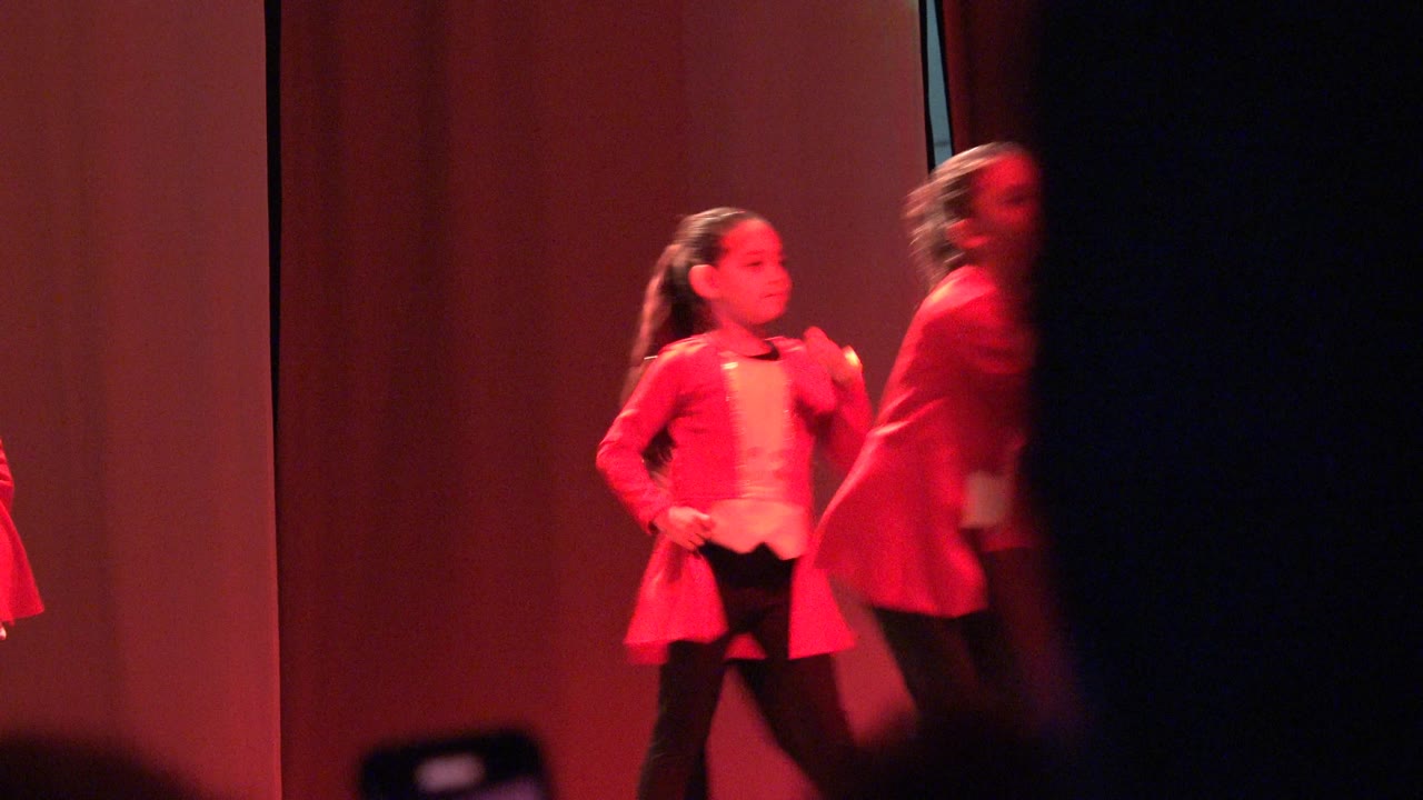 Children continue a stage dance routine in red costumes.
