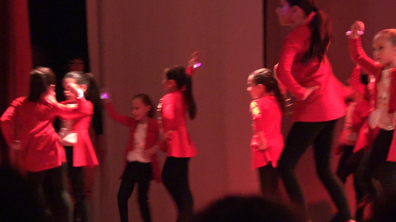 Children continue a synchronized dance routine under red stage light.