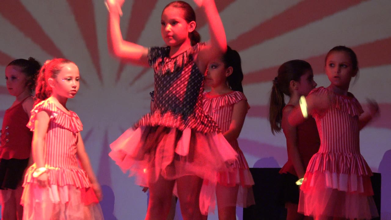Young girls perform on a stage in San Jose del Cabo BCS Mexico, with pink costumes, a dark polka-dot dress, and a red and white striped backdrop.