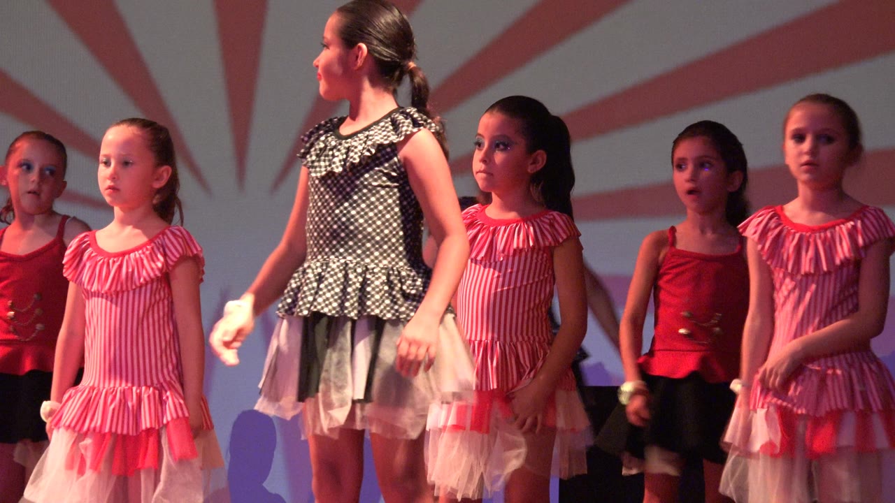 Children in pink and red costumes standing under stage lights.