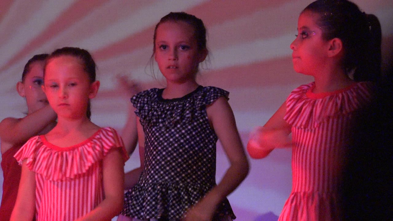 The San Jose Del Cabo BCS Mexico performance continues with a girl in a pink striped dress in profile, a darker silhouette in the foreground, and other children behind her.