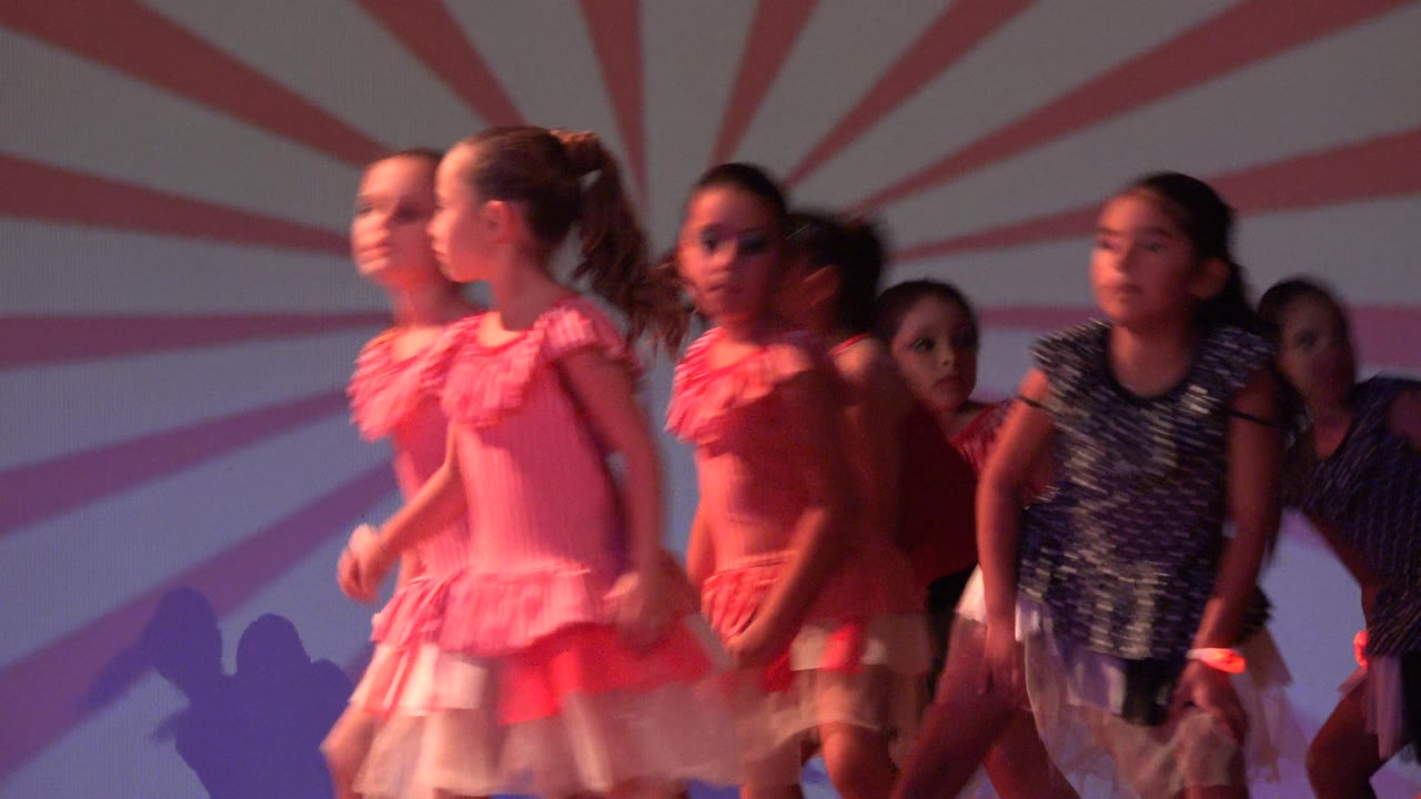 Children dancers moving across a stage under red lighting