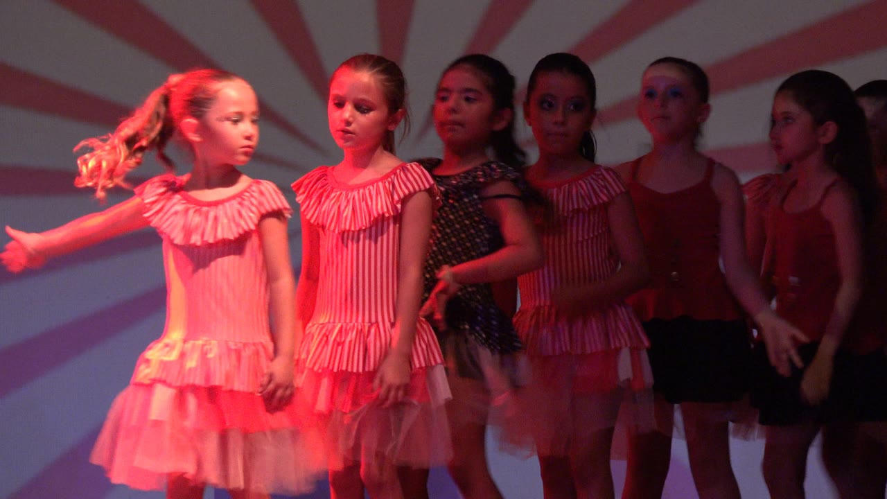 Girls in San Jose del Cabo, Mexico hold a staged formation, with one dancer extending her arm while others wait behind her in red and pink costumes.