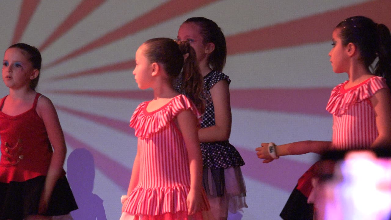 Girls on stage begin moving their arms during a dance routine.