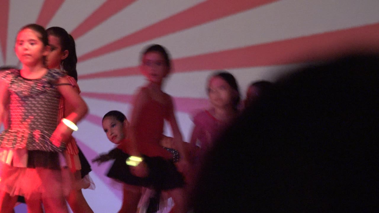 At 0:02 in San Jose Del Cabo BCS Mexico, girls in dance costumes move across the stage as a dark foreground silhouette blocks part of the lower frame.