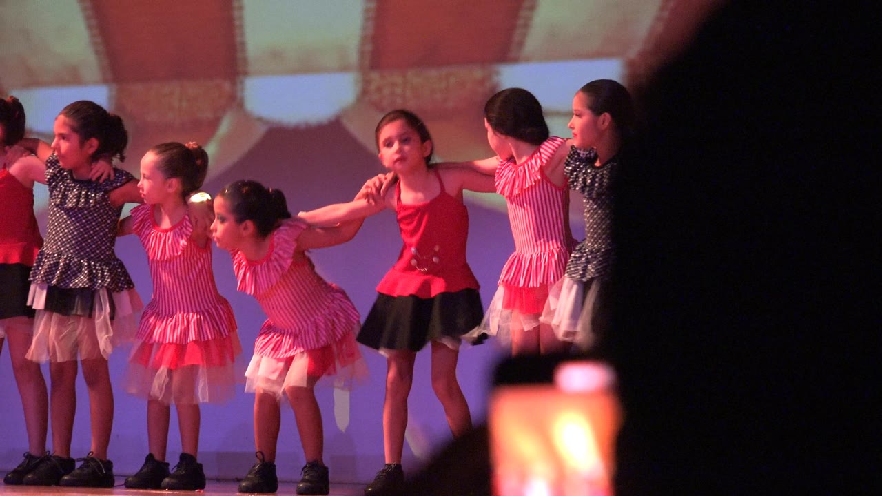 Children standing in a line on stage with arms across each other's shoulders.