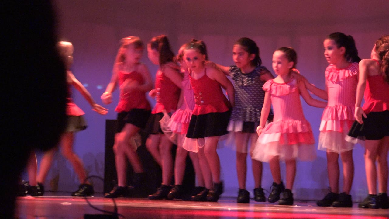 Girls begin moving across the stage with a dark audience silhouette in front.