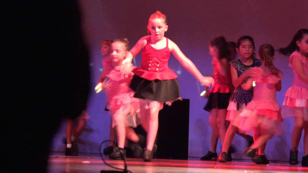 A girl in a red top and black skirt steps forward during the San Jose Del Cabo BCS Mexico stage routine as other girls move behind her.