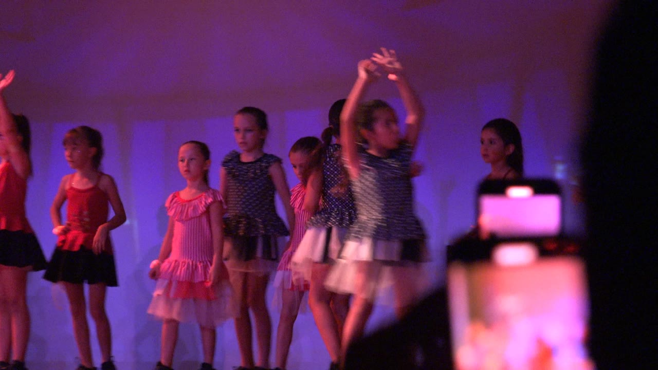 The dance group continues in San Jose Del Cabo BCS Mexico, with several girls lined across the stage and dark audience silhouettes cutting into the frame.