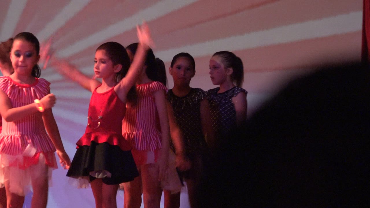 Girl in red top raises her arm beside other dancers.