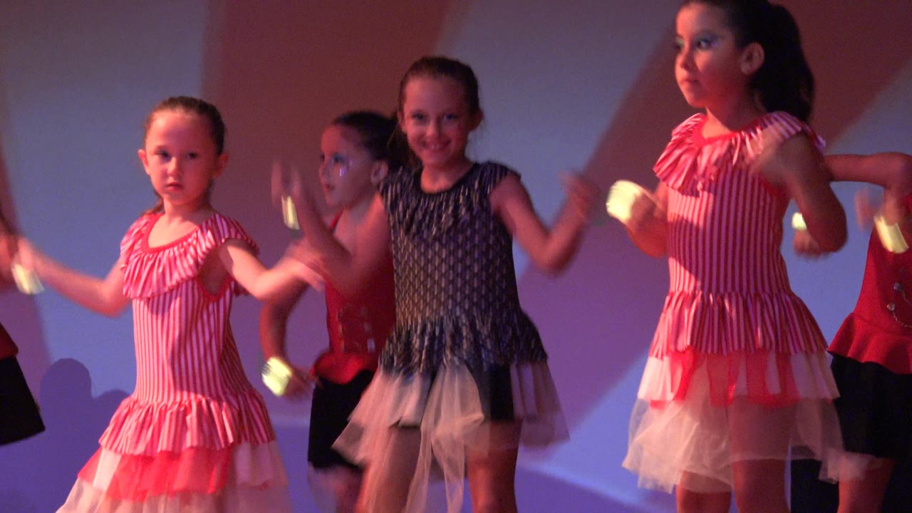 Girls in colorful dance costumes face forward on stage.