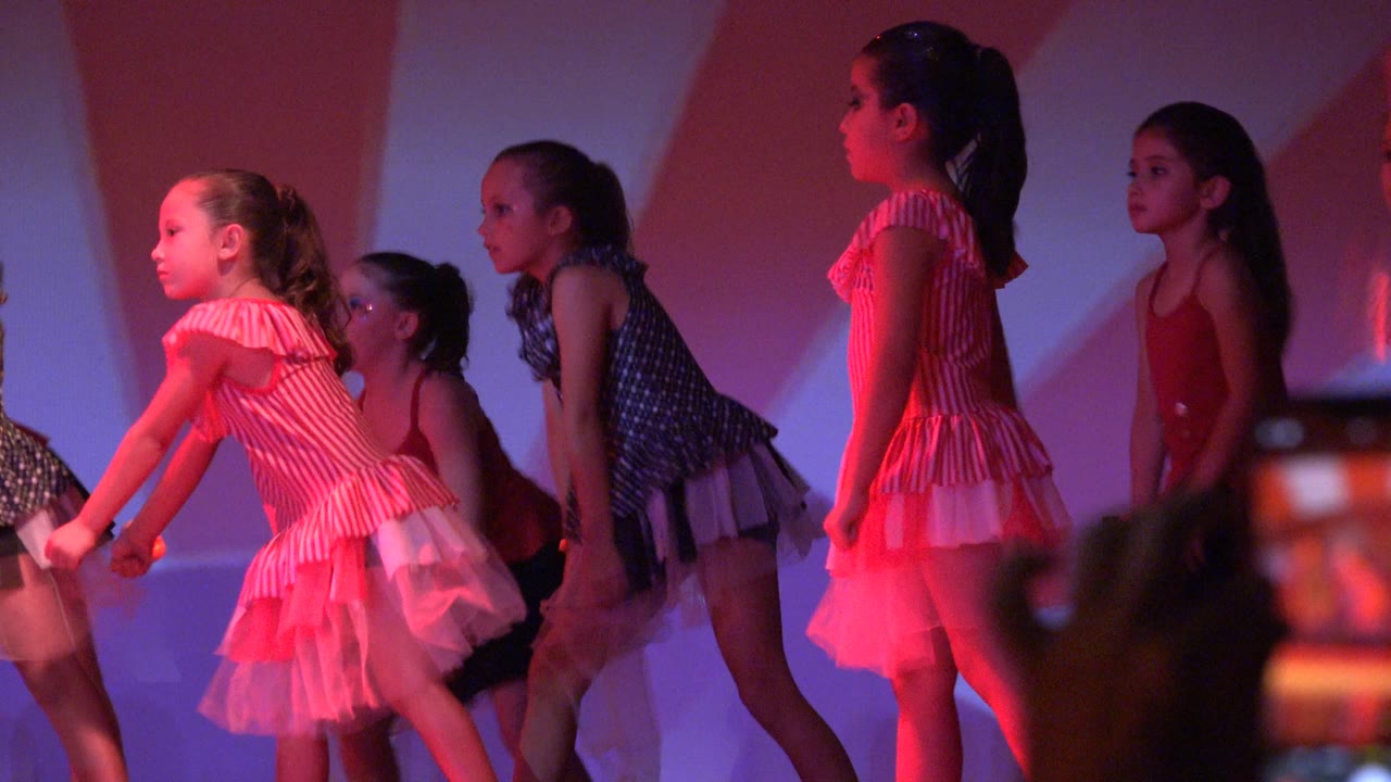 Young girls in layered pink, red, and black dance outfits perform on stage in San Jose Del Cabo BCS Mexico, with some motion blur and shadows on the backdrop.