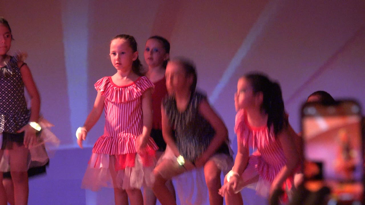 Girls in colorful dance costumes stand and crouch on stage.