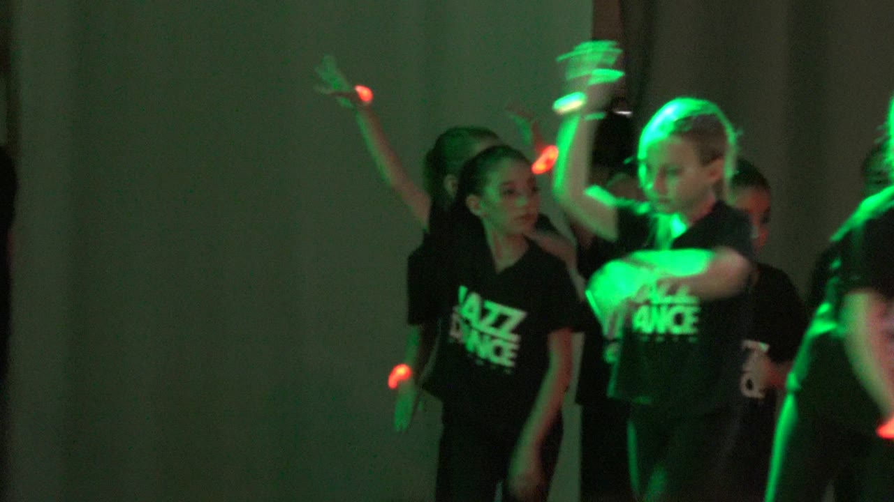 Children in black Jazz Dance shirts perform on a stage in San Jose del Cabo BCS Mexico, with green light on their arms and a curtain behind them.