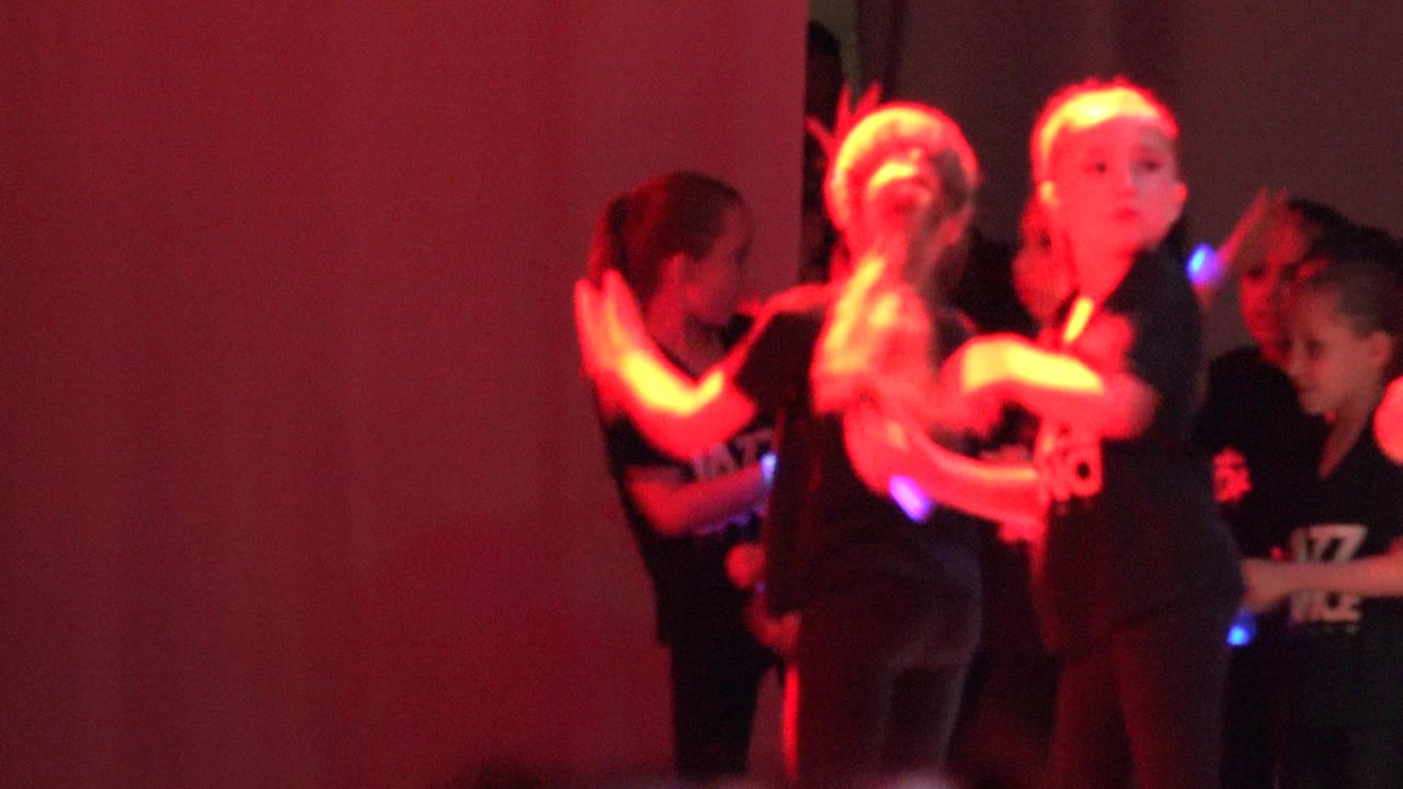 Children dancing in red stage light with glowing accessories.