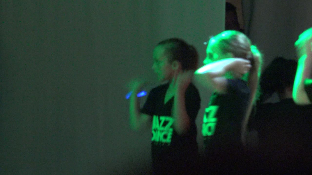 Children in black Jazz Dance shirts dance in San Jose del Cabo, Mexico while green light highlights raised arms and cropped figures at the right edge.