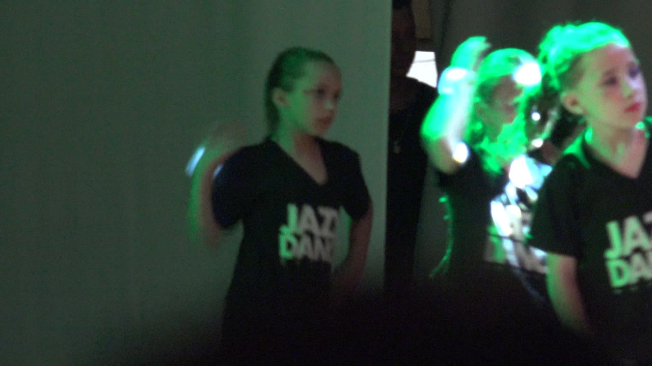 Children in black Jazz Dance shirts perform near a plain wall in San Jose del Cabo, Mexico, with green light on their faces and arms.