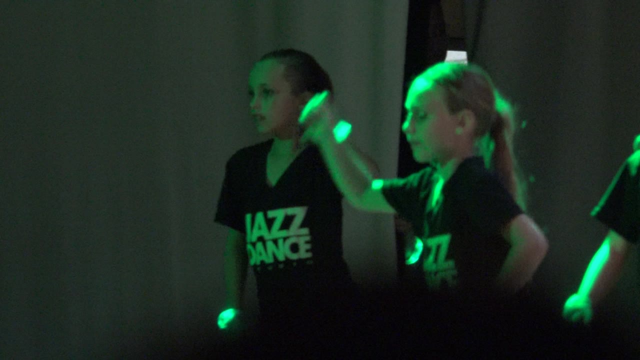 Two young dancers in black Jazz Dance shirts face sideways in San Jose del Cabo, Mexico, with green highlights on their faces, shirts, and arms.