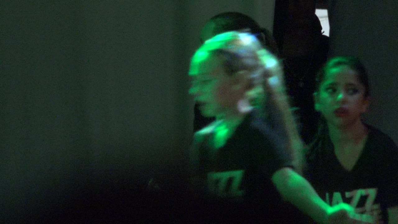 A child in a black jazz dance shirt in San Jose Del Cabo, Mexico is lit by red and green glow-stick colors while another child is partly visible at the edge.