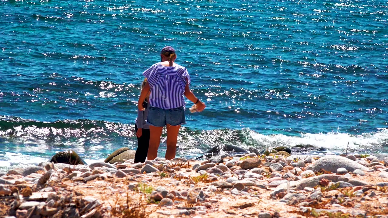 In El Sargento La Ventana Mexico, the adult and child stand close together on the rocky beach with small white waves rolling in behind them.