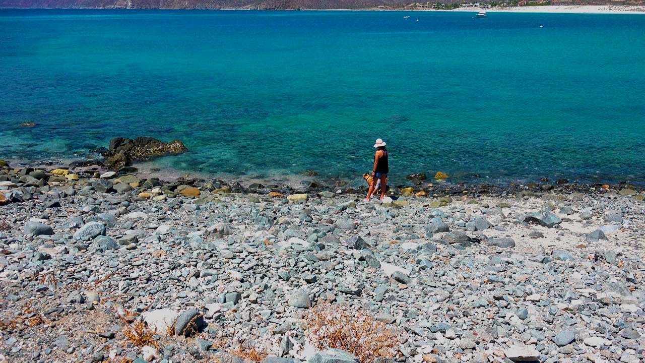 Adult and child farther along the pebbly beach near turquoise water.