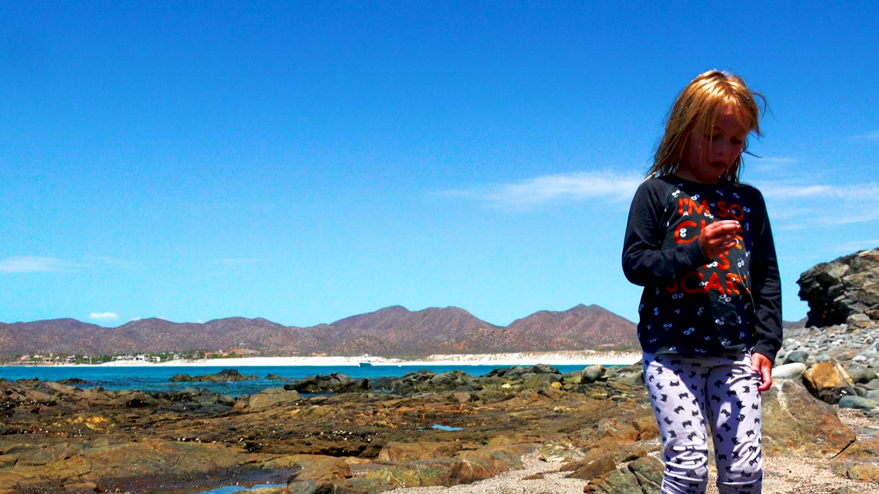 Child looking down while standing on rocks near the ocean.
