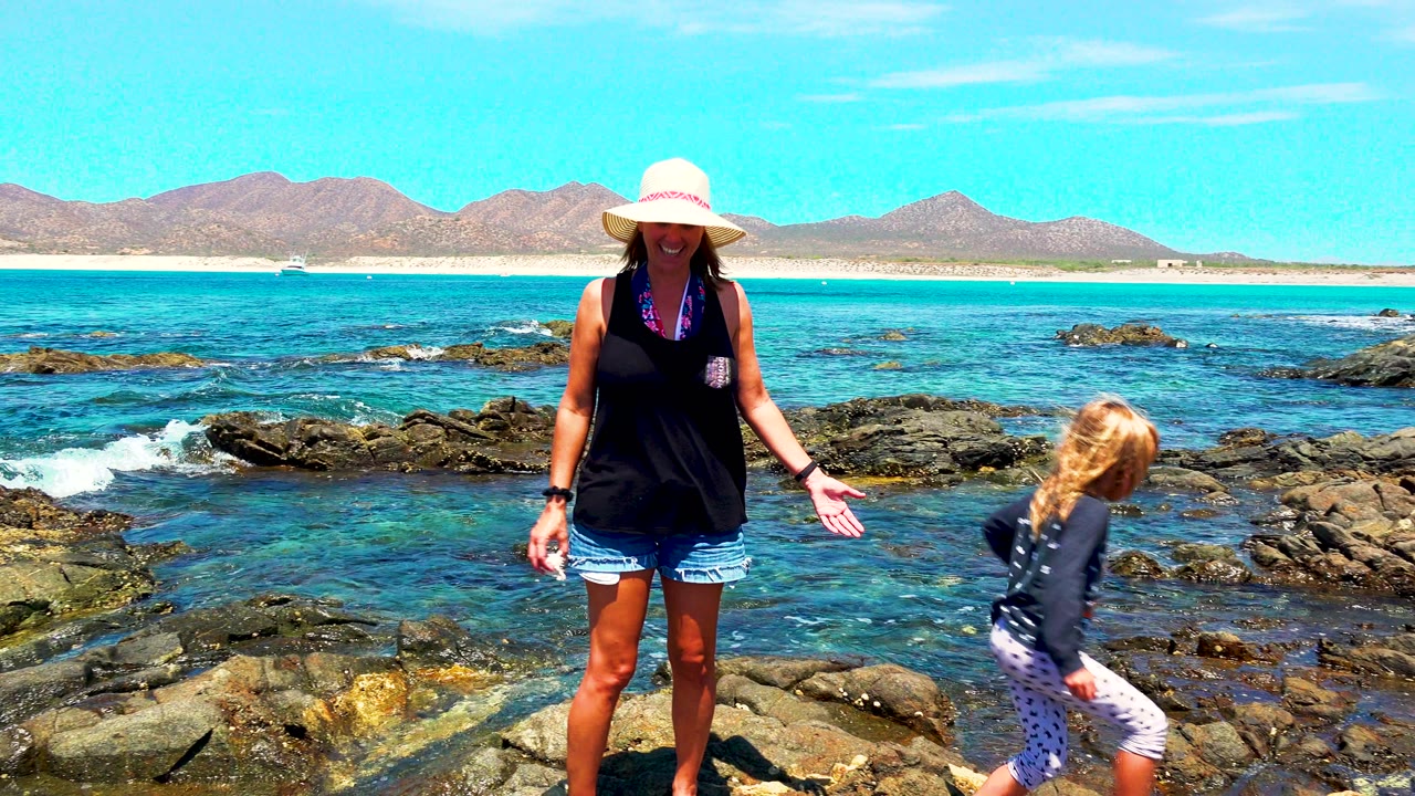 Woman facing the child on rocks with blue ocean behind.