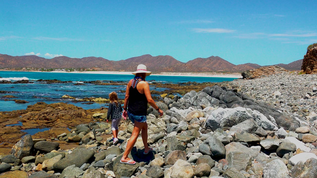 Woman and child walking over rocks near tide pools and ocean.