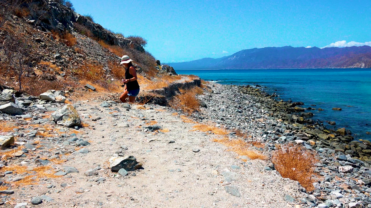 Woman walking along dry coastal trail above rocky shore
