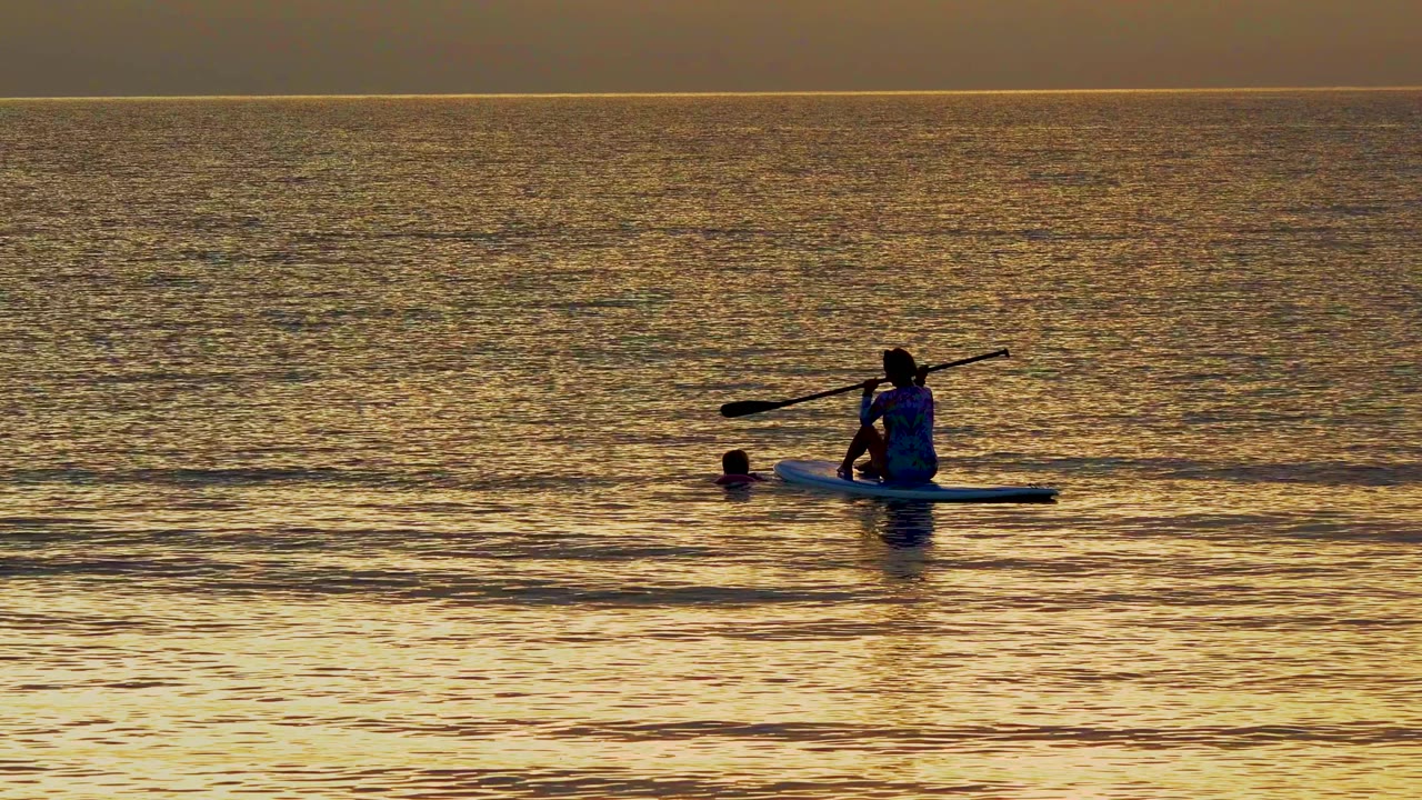 At 0:00 in El Sargento La Ventana Mexico, a silhouetted paddleboarder sits left of center on golden water while a swimmer's head appears beside the board.