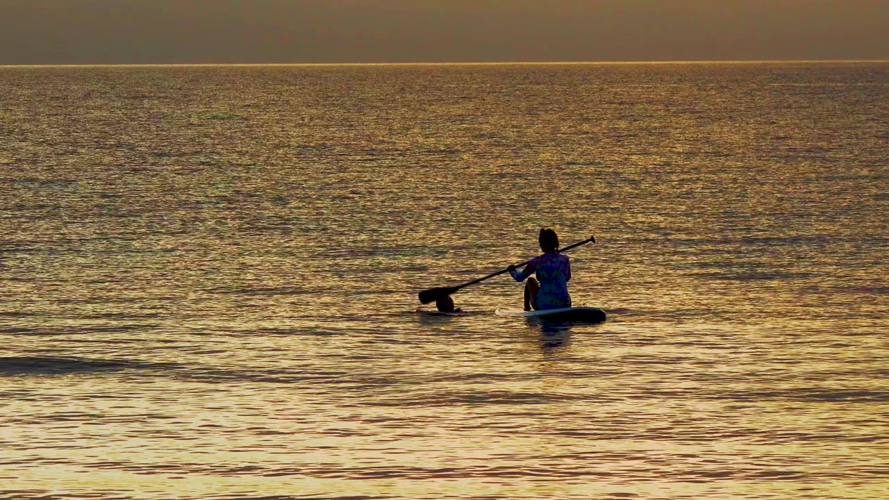 At 0:02 in El Sargento La Ventana Mexico, the paddleboarder appears near the right side of the wide frame with the paddle raised and the swimmer trailing to the left.