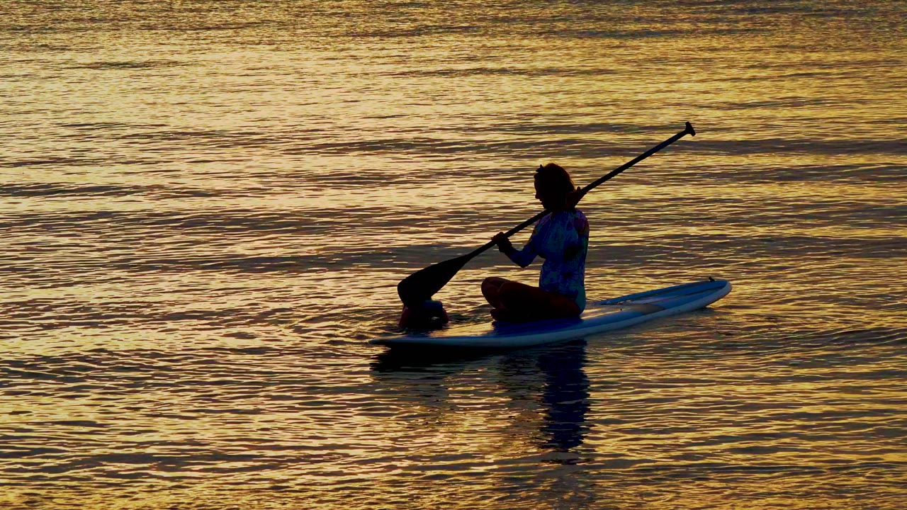 Paddleboarder dipping a paddle as a child swims nearby