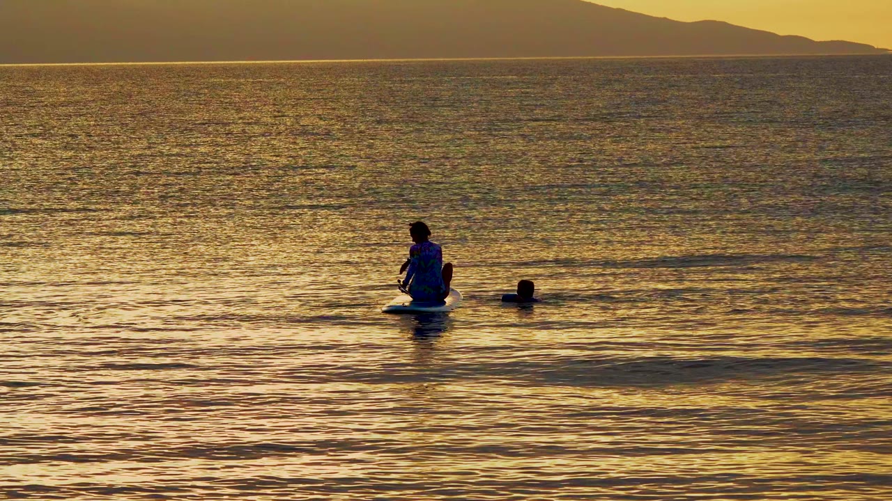 Person seated on a water float near a swimmer in golden water