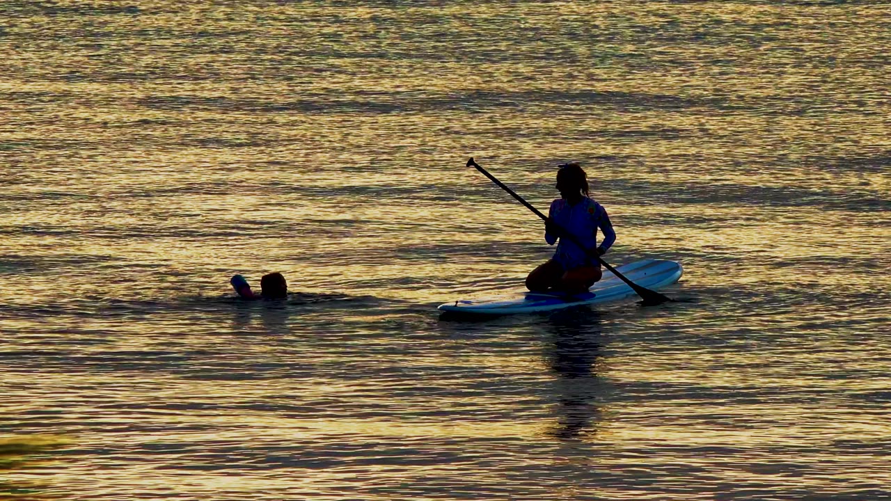 At 0:00 in El Sargento La Ventana, Mexico, a kneeling paddleboarder faces left while a swimmer floats nearby in gold-reflected water.