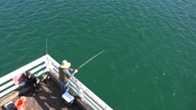 MALIBU CALIFORNIA-2020: A Man Wearing A Hat Fishing From The Corner Of A Deck