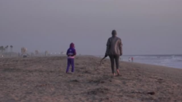HUNTINGTON BEACH CALIFORNIA-2020: An Adult And A Child Walking On The Beach Of