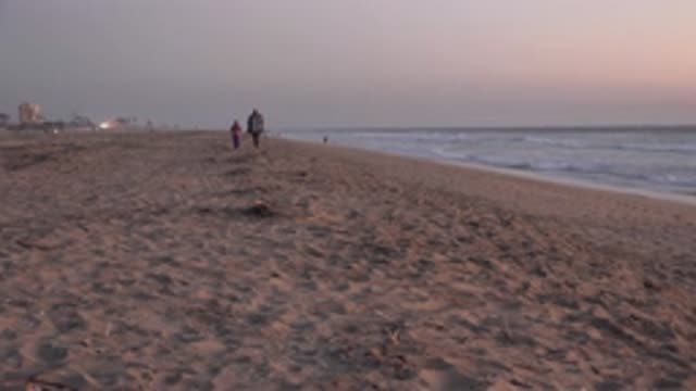 HUNTINGTON BEACH CALIFORNIA-2020: Two People Walking Toward The Camera On A Beach At Sunset