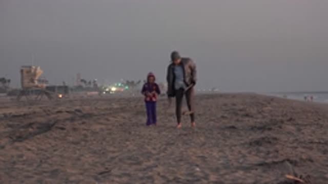 HUNTINGTON BEACH CALIFORNIA-2020: Man And Boy Stroll Along The Beach The Man Is Carrying Sticks