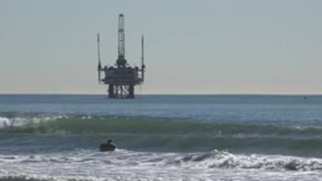 HUNTINGTON BEACH CALIFORNIA-2020: Man Lying On A Surfboard In Surf With An Oil Rig