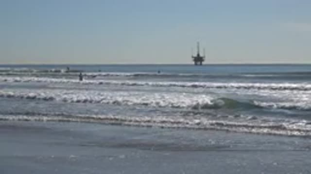HUNTINGTON BEACH CALIFORNIA-2020: An Oil Rig Is In The Distant Ocean While A Group Plays On The Beach