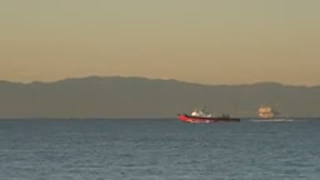 HUNTINGTON BEACH CALIFORNIA-2020: Red Boat Moves Across A Body Of Water During Sunrise