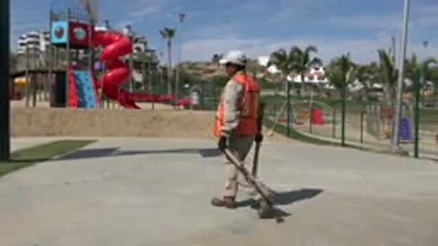 LOS CABOS MEXICO-2019: Groundskeeper Walking Through A Park Which Contains A Red Slide