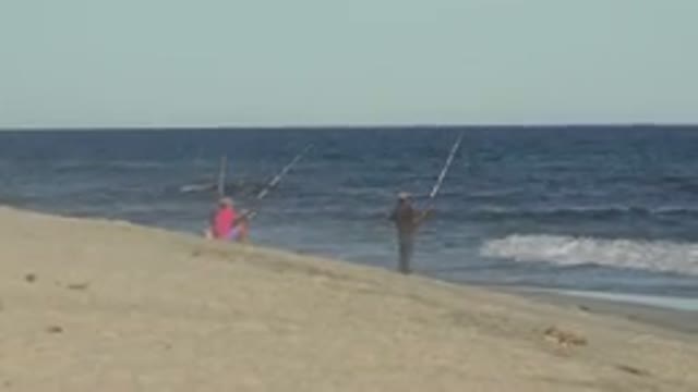 LOS CABOS MEXICO-2019: Two People Fish On A Beach With Long Fishing Rods While