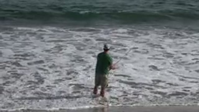 LOS CABOS MEXICO-2019: A Man Fishing In The Sea Eating Shorts And A Hat As The