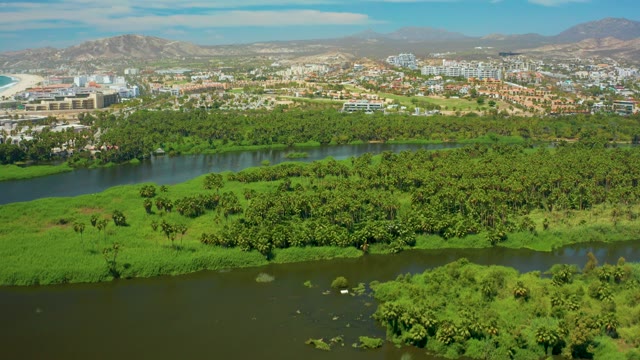 SAN JOSE DEL CABO BCS MEXICO-2021: River Winding Through Lush Greenery with Urban Backdrop