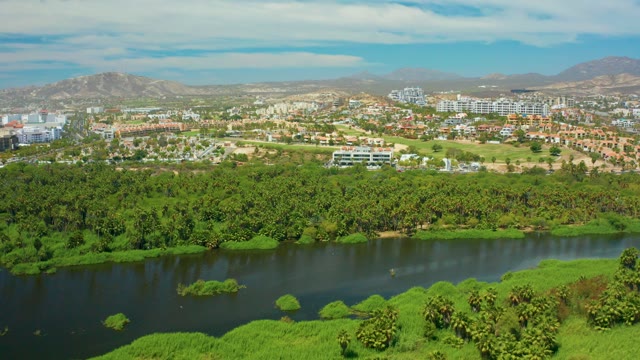 SAN JOSE DEL CABO BCS MEXICO-2021: River Flowing Through Lush Green Area with Town in Background