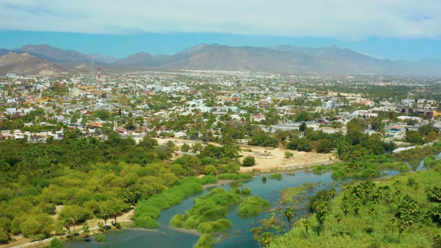 SAN JOSE DEL CABO BCS MEXICO-2021: River Winding Through Green Urban Landscape with Distant Mountains