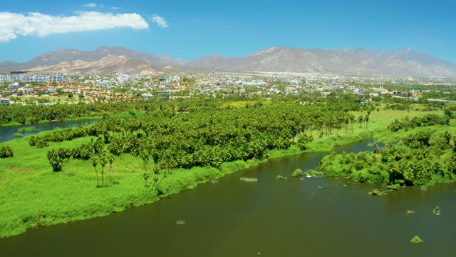 SAN JOSE DEL CABO ESTUARY BCS MEXICO-2021: River Flowing Through Green Landscape with City Beyond